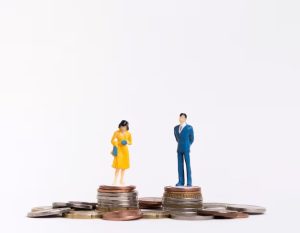Miniaturas de homem e mulher em cima de pilhas de moedas representando desigualdade salarial.